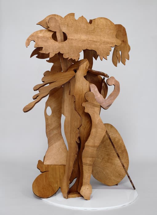 Freestanding wooden sculpture by Rachel Feinstein composed of layered cutouts forming abstracted human and tree-like shapes, displayed against a neutral background.