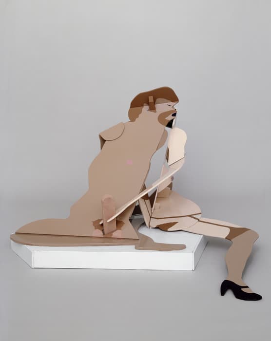 Sculpture of a stylized female figure, made of flat painted cutouts in shades of beige, brown, and pink, kneeling on one leg with the other extended forward, wearing black high heels, set against a plain gray background.