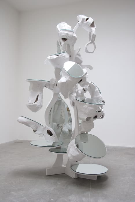 Abstract white sculpture by Rachel Feinstein with irregular organic shapes, embedded round mirrors, and hollow cavities, displayed in a minimalist gallery space.