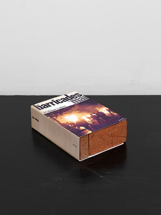 E HAUSSMANNIZATION, BARRICADE FIGHTING 

Claire Fontaine, Les barricades de mai brickbat, 2007
Brick, brick fragments, digital print
Courtesy of the artist

The period between 1830 and 1848 saw seven armed popular uprisings in Paris, with insurgents repeatedly building barricades in the city’s narrow medieval streets. In an effort to safeguard against future rebellions and to improve sanitation, the government of Napoléon III commissioned Baron Georges-Eugène Haussmann to modernize the center of Paris. Haussmann transformed the city, carving wide, straight boulevards through its tangled heart.

Still, Paris remained a hotbed of revolution. The Communards seized control of parts of the city in 1871; in May 1968, more than a century after Haussmann’s intervention, students and workers built their own barricades during strikes and sit-ins against the conservative government of Charles de Gaulle.

Claire Fontaine’s brickbats refer to such protests, wrapping the classic street weapon in the jacket of a book. The work calls into question the maxim that the pen is mightier than the sword, giving physical form to the debate between political movements based on intellectual persuasion and those that rely on direct action.