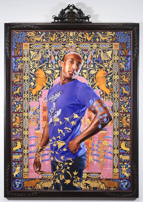 Portrait of a man in a purple shirt standing confidently with one hand on his hip, set against an ornate, colorful backdrop featuring intricate gold floral patterns, animals, and architectural motifs framed in black with a decorative top ornament.