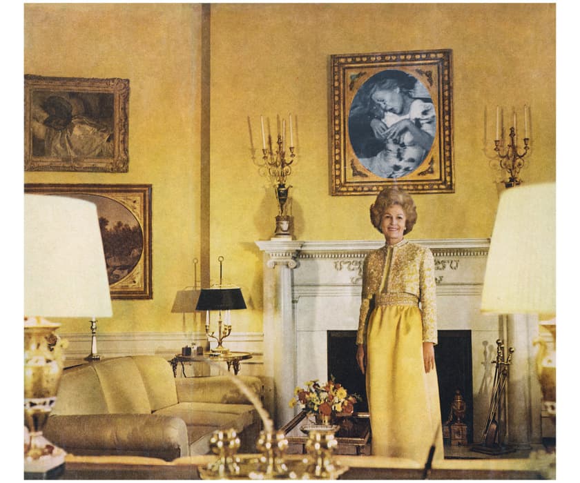 A woman in a yellow gown stands smiling in an opulent, yellow-toned living room with antique furniture, ornate candelabras, and a white fireplace topped with a framed black-and-white portrait.