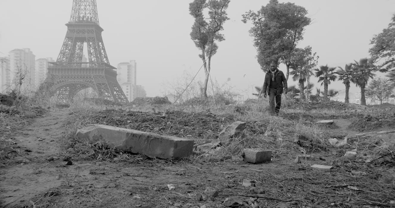 C ANCIENT PARIS, CATACOMBS, DEMOLITIONS, DECLINE OF PARIS 

Jesper Just, Intercourses, 2013
Modified 5-channel video installation
Courtesy of the artist and Galerie Perrotin, New York

In The Arcades Project, Walter Benjamin both describes and contributes to the mythology of Paris. He reflects on the astonishing volume of writing that has been devoted to “the investigation of this tiny spot on the earth’s surface,” from its buried antiquities to its bordellos.

Jesper Just’s video records a recent contribution to this history of fascination: a residential development in suburban China wth mansard-roofed apartment blocks, a mini Champs-Elysées, and a copy of the Eiffel Tower. Though it was intended to house ten thousand people, the cheaply built replica city is sparsely populated and already crumbling. Staircases lead to fields strewn with construction debris; weeds surround the Eiffel Tower. This hard-luck doppelgänger fulfills dystopian fantasies of the demise of a great city.