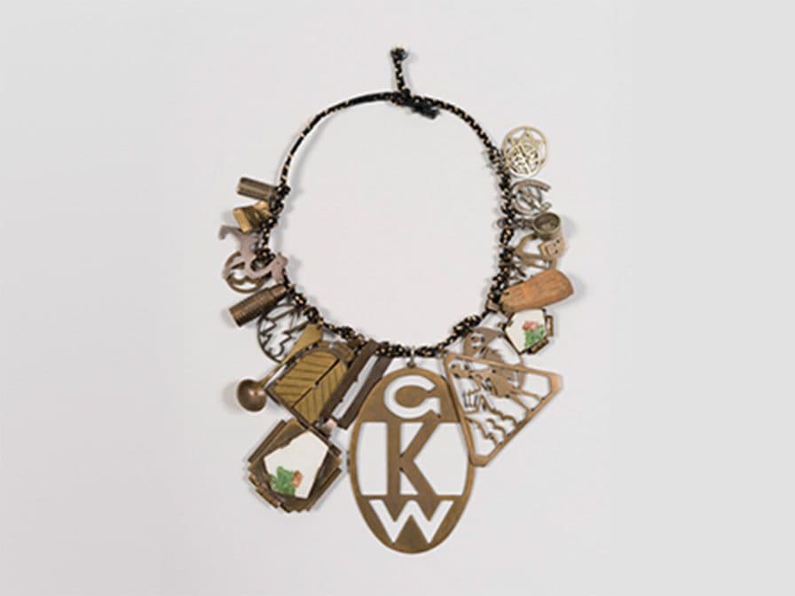 Necklace with various charms made of metal, wood, and ceramic, featuring letters, symbols, and small objects, including a large central pendant with the initials 