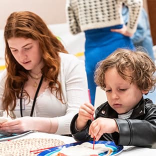 Teen and child seated at a table, focused on hands-on art activities with modeling clay and paint.