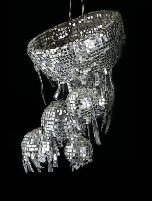 Hanging sculpture made of fragmented mirror tiles forming a large basket-like structure with multiple disco-ball shapes dangling below, set against a black background.