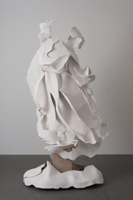Large white sculpture by Rachel Feinstein depicting a layered, flowing, abstracted female figure with draped garments and sweeping curves, standing on a textured base.