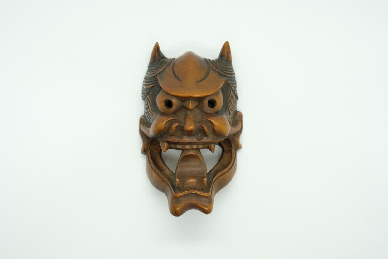 Small carved wooden mask with a fierce expression, open mouth, fangs, and two horns.