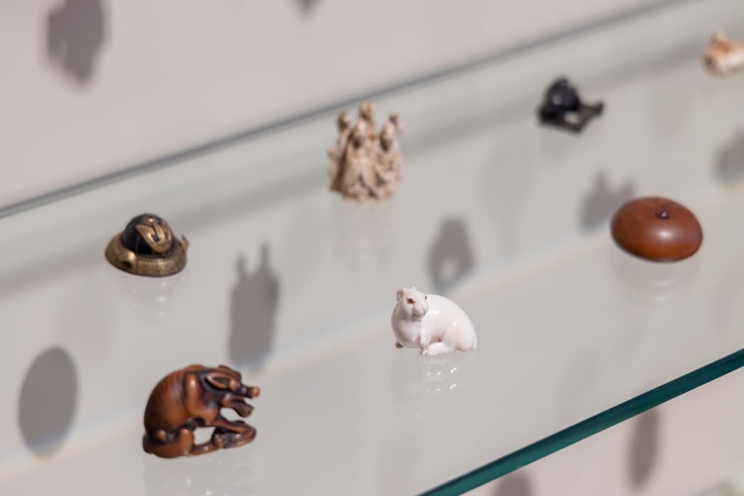Close-up of small netsuke sculptures, including a white rabbit, displayed on a glass shelf.
