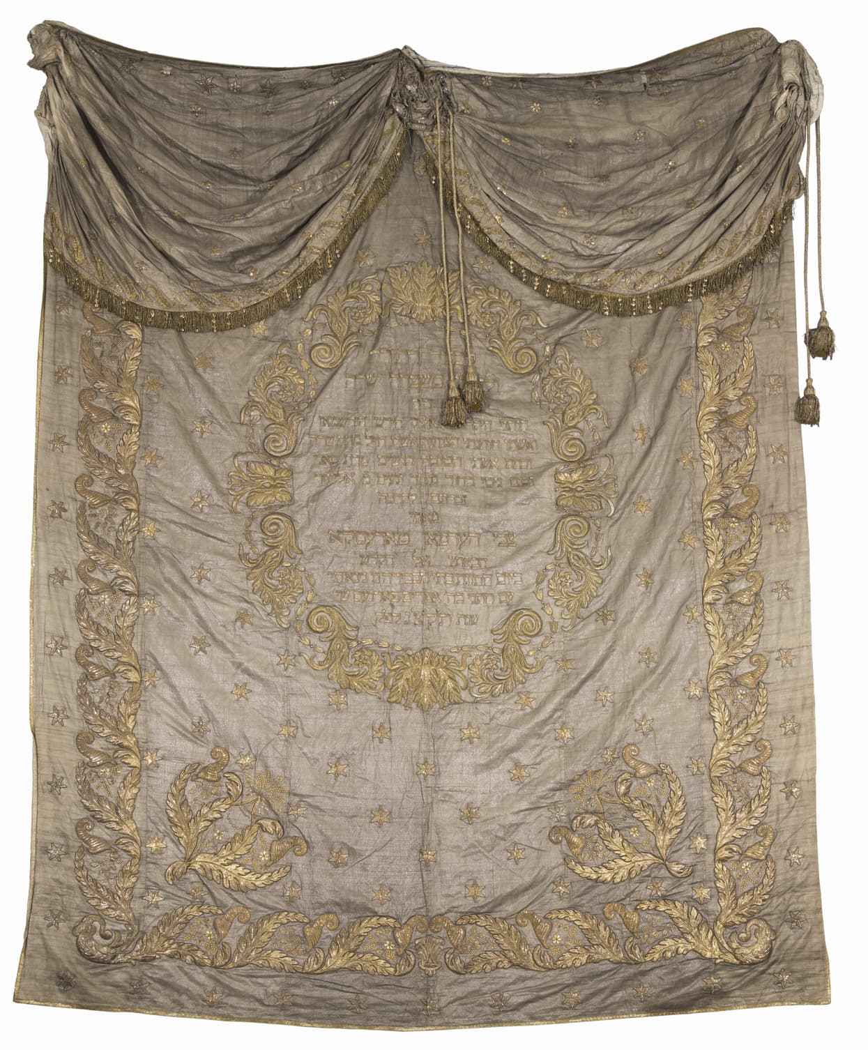 Ornate embroidered Torah ark curtain with gold floral designs, Hebrew text, and decorative swags at the top.