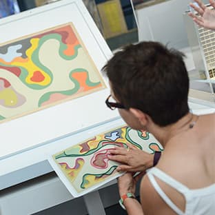 A program participant runs her hand over a raised-line image of a landscape by Roberto Burle Marx. The original is in front of her.
