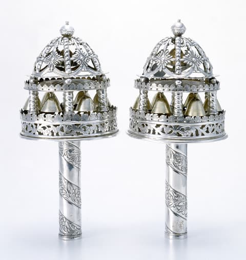 Pair of ornate silver Torah finials with domed, openwork tops, small bells hanging inside, and decorative spiral handles.